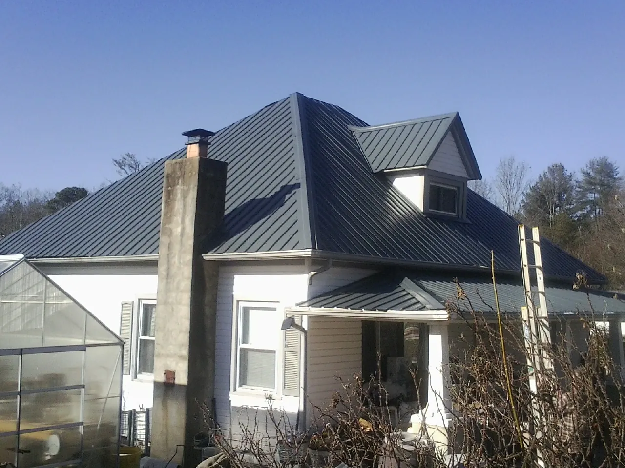 Dark blue standing seam metal roof on a white farmhouse with dormer — Slate & Tile Roof Repair by Roofing Brothers in Martin City