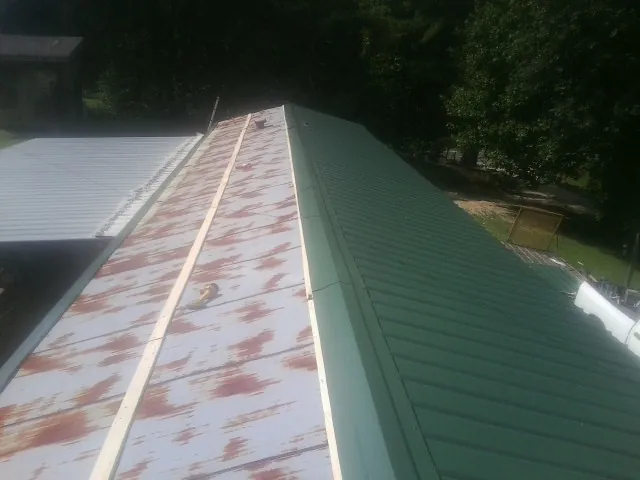 Old rusted panels beside newly installed green metal roofing — Wind Damage Roof Repair by Roofing Brothers in Martin City