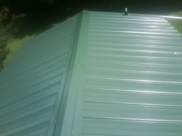 New green metal panels meeting at the ridge of a roof — Flat Roof Repair work by our crew in Martin City