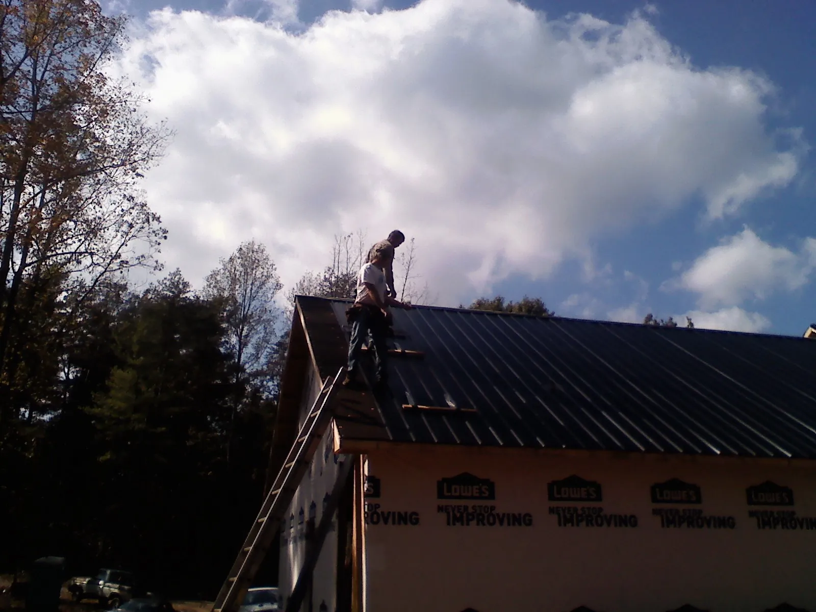 Roofer fastening dark metal panels high against a cloudy sky, from a Roof Inspection job in Martin City