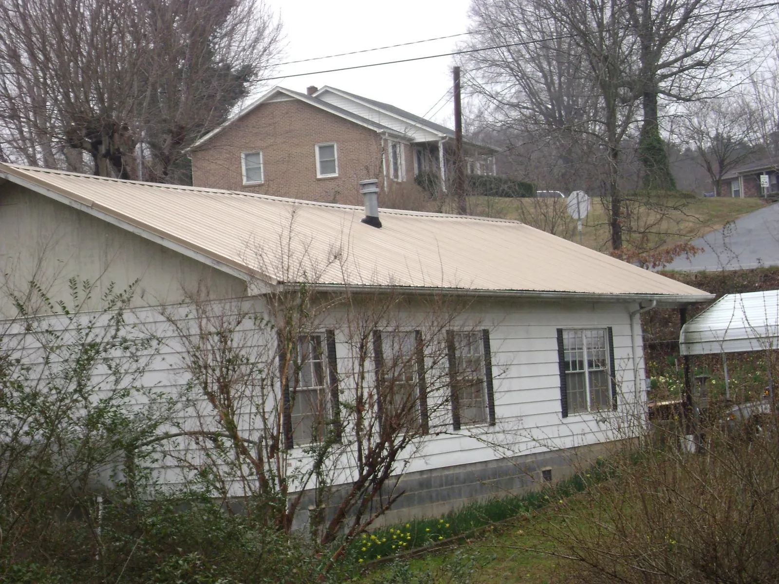 Tan metal roof on a white sided house set into a hillside — Commercial Roofing by Roofing Brothers in Martin City