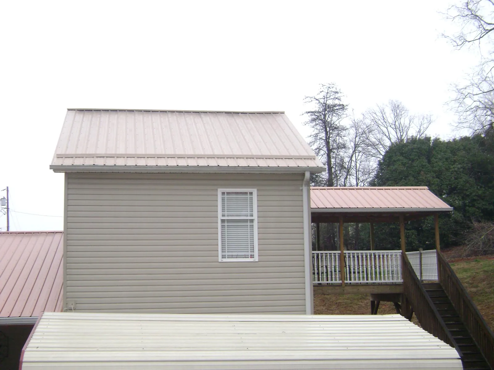 Tan metal roofs on a two story addition and attached porch, from a Roof Replacement job in Martin City